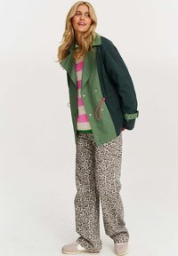 Zeleno-námořnický dvouřadý blejzr s růžovým stahovacím šňůrkou, pruhovaný svetr v růžové a béžové barvě a široké kalhoty s leopardím potiskem.