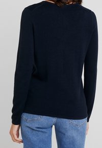 Donkerblauwe langemouwen trui van zachte stof, met een ronde hals en geribbelde manchetten, gecombineerd met lichtblauwe jeans.