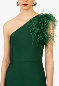 Groene jurk met één schouder, voorzien van een gestructureerd oppervlak en een grote veeraccent op de schouder. Heeft een getailleerd lijfje.