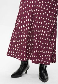 Gonna bordeaux con pois bianchi, realizzata in tessuto morbido, abbinata a stivaletti neri lucidi a punta con tacco alto.