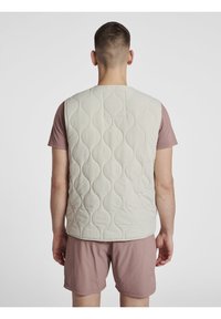 Light gray quilted vest with a rounded pattern, sleeveless design, and a small back pocket, worn over a pink T-shirt and shorts.