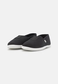 Sapatilhas pretas em lona, tipo slip-on, com biqueira arredondada, sola de borracha branca e detalhes em borracha elástica para fácil calçar. Design simples e leve.