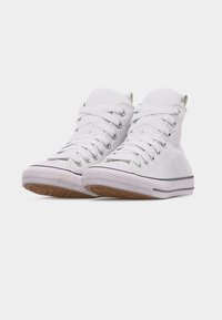 Ζευγάρι λευκά ψηλά πάνινα αθλητικά παπούτσια με λευκά κορδόνια και λαστιχένιες σόλες, τοποθετημένα σε ελαφρώς κεκλιμένη γωνία πάνω σε απλό λευκό φόντο.