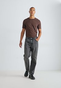 Brown short-sleeve T-shirt paired with gray denim jeans and black shoes. Simple design, relaxed fit, and smooth fabric texture.