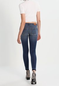 Jeans de mezclilla ajustados en un tono azul oscuro con bolsillos traseros, combinados con botas de plataforma de print animal en blanco y negro. Textura lisa.
