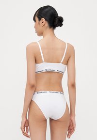 White bikini top and bottom with black "Juicy Couture" logo waistband. Stretchy fabric, adjustable straps, and basic design.