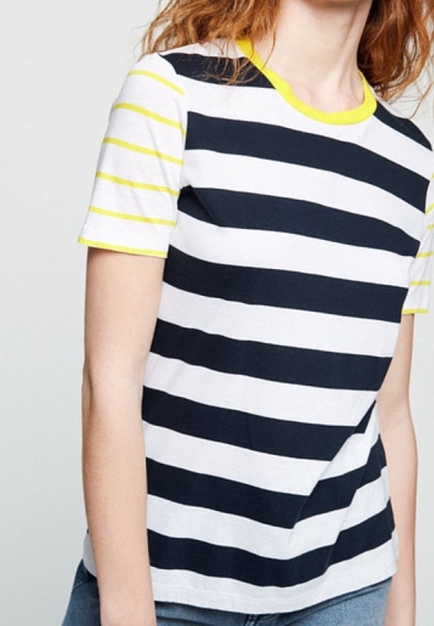 Personne portant une chemise à manches courtes avec de larges rayures horizontales noires et blanches ainsi que des manches et un col rayés jaunes.