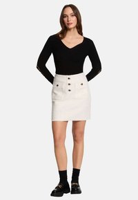 Haut noir à manches longues avec un col en V, associé à une jupe en denim blanche avec des boutons sur le devant, deux poches et une coupe ajustée.