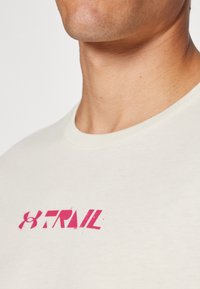 Ljus beige bomull t-shirt med en rosa tryckt logotyp, rund halsringning och korta ärmar, designad för komfort och avslappnad stil.