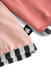Zwei Stoffhüllen, eine in sanftem Rosa und die andere in gedämpftem Koralle, mit einem schwarz-weißen karierten Akzent. Ein kleines schwarzes Etikett ist sichtbar.