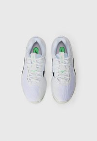 White athletic shoes with textured fabric, black accents, green logo, and laces. Features a cushioned sole and geometric design on the side.