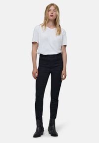 Vaqueros negros de cintura alta combinados con una camiseta blanca de manga corta y botas negras hasta el tobillo. Tela suave, silueta ajustada, estilo minimalista.