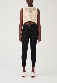 Crème gebreid cropped top met een ribbelpatroon, gecombineerd met hoge zwarte skinny jeans en lichtroze sandalen met open tenen en hoge hakken.
