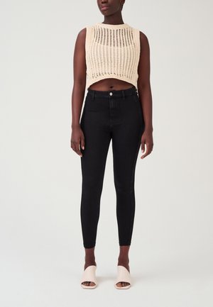 Top corto lavorato a maglia color crema con un motivo a costine, abbinato a jeans skinny neri a vita alta e sandali con tacco aperti color rosa chiaro.