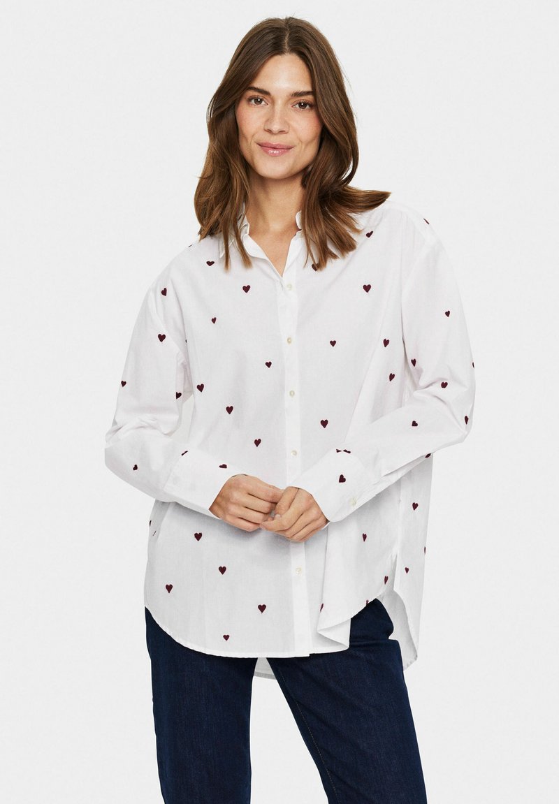 Camicia bianca con bottoni, decorata con motivi a cuore color bordeaux sparsi, maniche lunghe e orlo curvo. Realizzata in tessuto leggero.