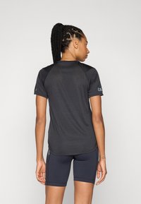 T-shirt de sport noir à manches courtes, en tissu texturé et à col rond. Présente un logo sur la manche gauche et des détails contrastés.