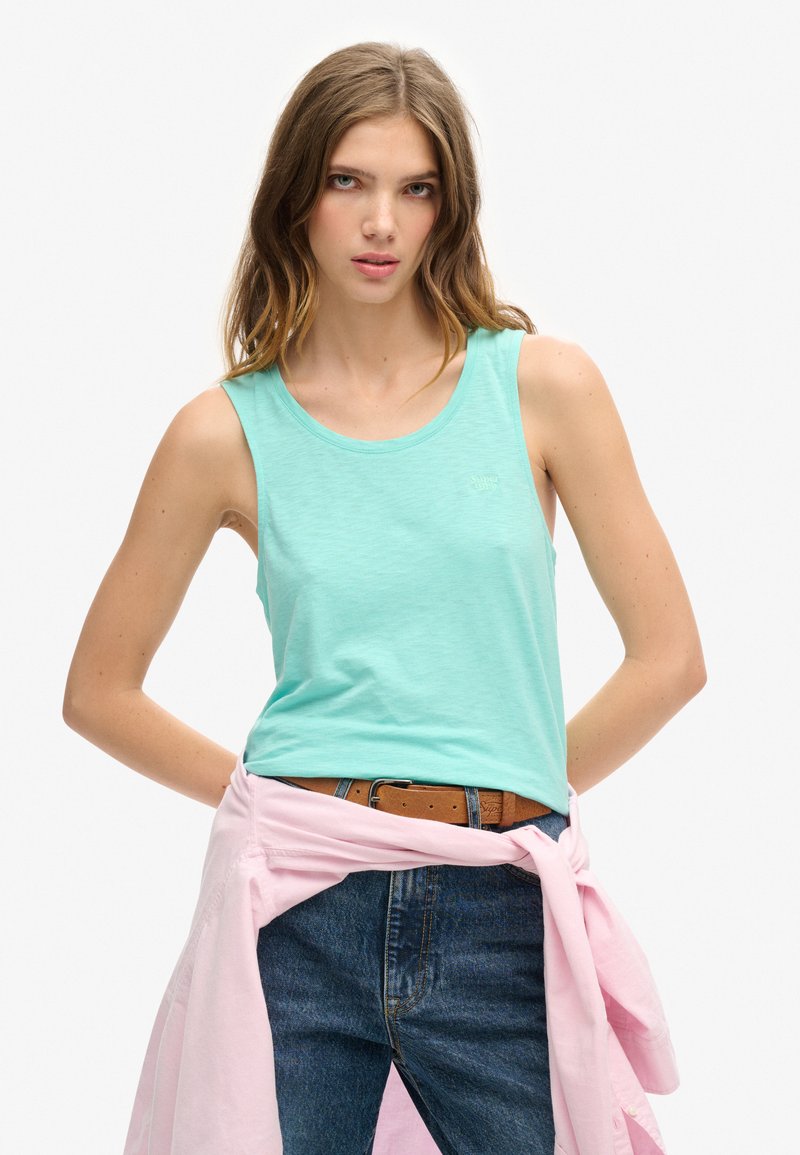 Canotta verde menta chiaro in morbido cotone, con scollatura rotonda e senza maniche. Abbinata a jeans a vita alta e una camicia rosa legata in vita.