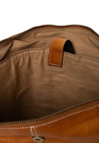 Interieur van een bruine leren tas met een gladde textuur, voorzien van een centrale rits en een leren lus voor gemakkelijke toegang of ophangen.