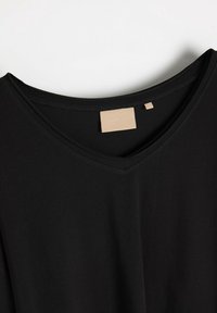 Czarny t-shirt z dekoltem w serek, wykonany z miękkiego materiału, z minimalistycznym wzorem i małą beżową metką przy dekolcie. Gładka faktura.