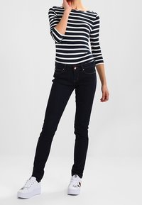 Granatowo-biały paskowany top z długim rękawem zestawiony z ciemnoniebieskimi dopasowanymi dżinsami, uzupełniony białymi sneakersami z metalicznymi akcentami.