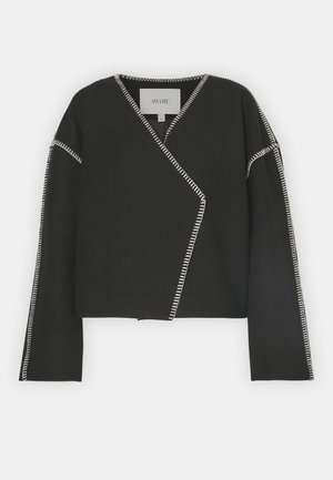 Veste noire en tissu doux avec des coutures blanches contrastantes, longueur cropped, décolleté en V profond et manches longues.