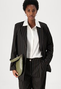 Black pinstripe suit with a white button-up shirt. The outfit features a green clutch with a handle, showcasing a sleek design and texture.