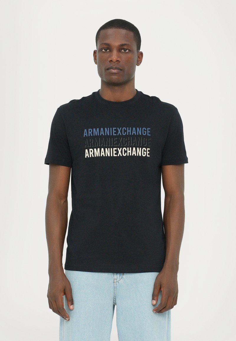Svart bomull T-skjorte med "ARMANIEXCHANGE"-tekst i blått, svart og kremfarge. Korte ermer og rund hals. Ledig passform.