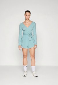 Top cruzado azul claro con mangas largas y pantalones cortos a juego, con cintura elástica y bolsillos laterales. Zapatillas blancas y calcetines.