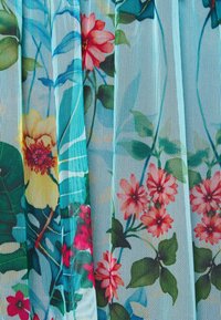 Tissu bleu transparent avec une texture en maille, orné de motifs floraux multicolores comprenant des fleurs jaunes, roses et rouges avec des feuilles vertes.