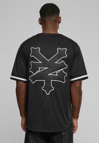 T-shirt noir à manches courtes avec une silhouette blanche d'un crâne et de poignards au dos. Présente des accents rayés sur les manches.