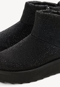 Schwarze Stiefeletten mit strukturierten, funkelnden Verzierungen, dicken Sohlen und seitlichen Reißverschlüssen für einfaches Anziehen.