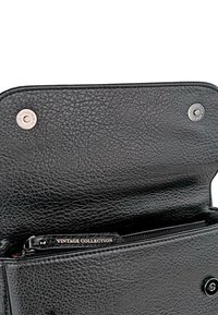 Cartera de cuero negro con un acabado texturizado, cierre a presión, bolsillo interior con cremallera etiquetado "COLECCIÓN VINTAGE" y detalles de herrajes metálicos.