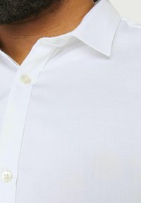 White dress shirt collar with a button closure. The fabric appears smooth with a slight sheen, featuring a pointed collar design.