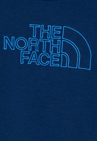 Navy blue cotton t-shirt featuring bold turquoise embroidered text of "THE NORTH FACE" with a curved logo accent.