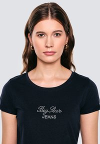 Námořnické tričko s kulatým výstřihem a krátkými rukávy; na přední straně zdobeno logem „Big Star JEANS“ z kamínků. Hladká struktura látky.