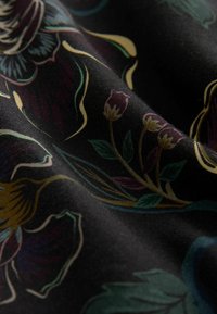 Floral-patterned fabric in dark black with colorful motifs of blooms and leaves. Smooth texture with vibrant colors, including gold and green accents.