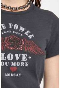 T-shirt noir en coton avec un motif de rose rouge avec des ailes, du texte blanc et des clous argentés. Encolure ronde et manches courtes.