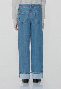 Džínové kalhoty širokého střihu v prostřední modré barvě se zesvětlenou texturou. Obsahují klasické kapsy a manžety s akcentem ze světlejšího denimu.