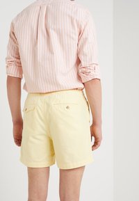 Světle růžová pruhovaná košile s ohrnutými rukávy, kterou doplňují pastelově žluté šortky s šňůrkou v pase a dvěma zadními kapsami.