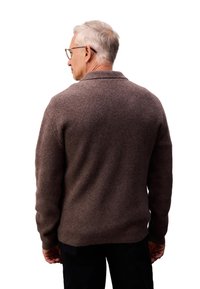 Bruine wollen trui met een sjaalkraag, geribde manchetten en een relaxte pasvorm. Gelaagd textiel, geen zichtbare patronen, gedragen over donkere broeken.
