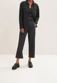 Grå stickad topp och matchande vida byxor, tillsammans med en mörk knapprad skjorta. Svarta loafers fulländar ensemblet.