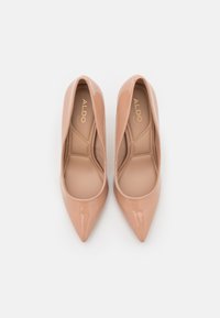 Escarpins en cuir verni beige à talons hauts avec un bout pointu et une ligne supérieure incurvée, présentant une surface lisse et brillante et une doublure intérieure subtile.