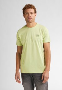 T-shirt di cotone verde chiaro con colletto rotondo e maniche corte. Presenta un piccolo logo circolare stampato sul lato sinistro del petto.