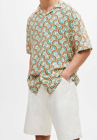 Short-sleeve shirt with an abstract pattern in orange, teal, and cream. Lightweight fabric, classic collar, buttons down the front.