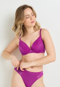 Soutien-gorge violette avec dentelle, accompagné d'un slip assorti, présentant un motif texturé, des bretelles réglables et un petit détail de bouton décoratif.