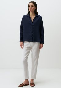 Camicia button-up in lino navy con colletto, abbinata a pantaloni in lino bianchi e sandali marroni con cinturini. Taglio semplice e rilassato.