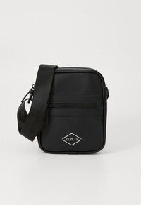 Bolso de hombro sintético negro con textura suave, que cuenta con un bolsillo frontal con cremallera y un logo en forma de diamante. Incluye una correa ajustable.
