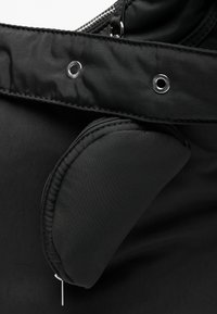 Zwarte stoffen tas met een ritssluiting, voorzien van een gewatteerde zijvak en een ronde metalen oogje detail bovenaan. Over het algemeen een gladde textuur.