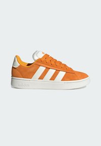 Zapatilla de Adidas de ante naranja con rayas, cordones y suela blancos, vista de lado sobre un fondo claro.