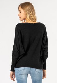 Black, oversized sweater with a loose fit, featuring a wide neckline and long sleeves. Soft texture, minimalistic design.